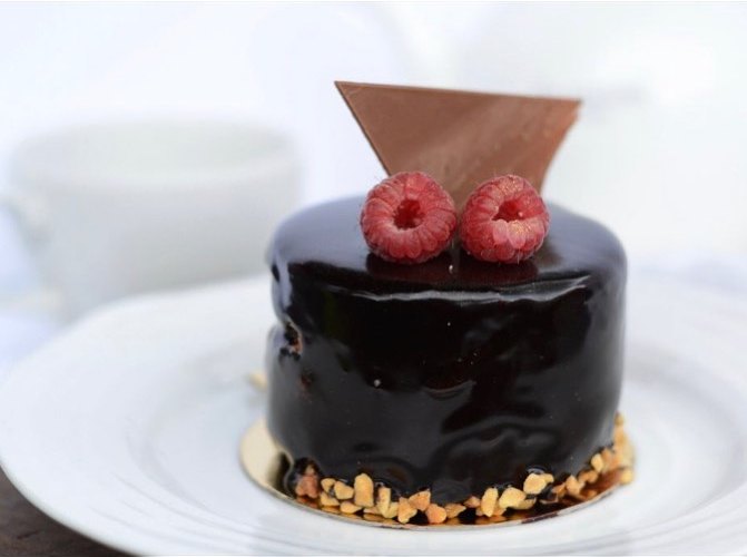 A glossy dark chocolate individual cake with two raspberries and a chocolate shard