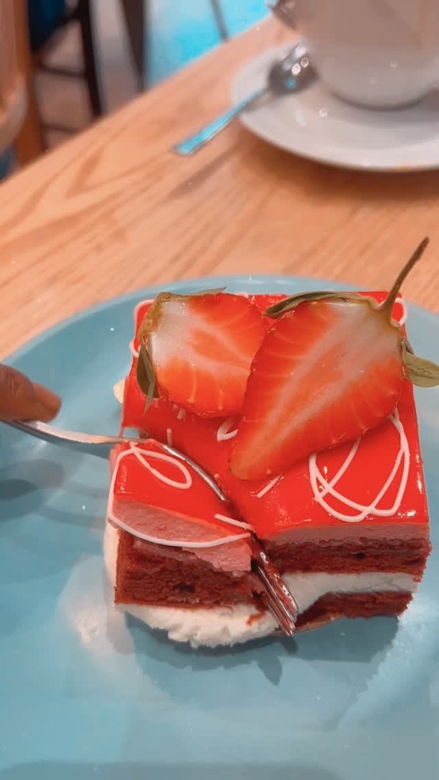 A fork lifting a bite from a slice of red velvet cake on a blue plate